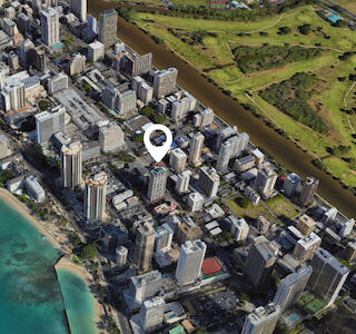 Aerial view of a coastal city with tall buildings, adjacent to a turquoise ocean and a golf course. A marker pinpoints a location in the city.