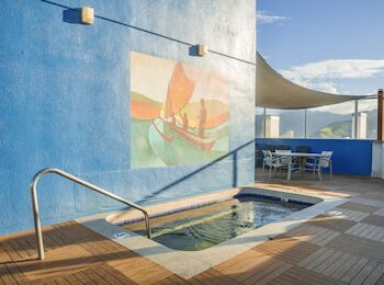 This image shows a small pool on a rooftop deck with a blue painted wall and a mural of a boat, accompanied by patio furniture.