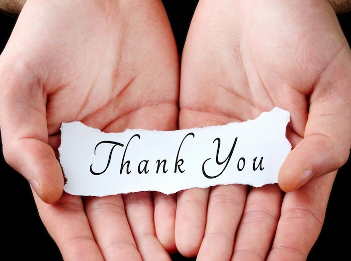 Two hands are holding a torn piece of paper that has "Thank You" written on it in elegant script.