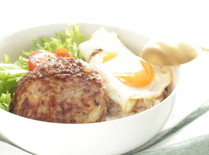 A bowl with a hamburger patty, fried egg, green lettuce, cherry tomatoes, and rice is displayed.