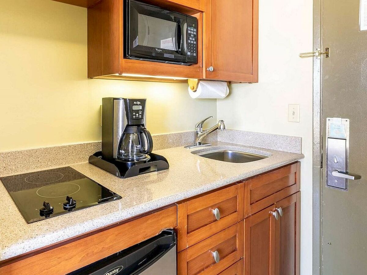 A small kitchenette with a microwave, coffee maker, electric stovetop, sink, and cabinets. It appears compact and efficient for basic use.