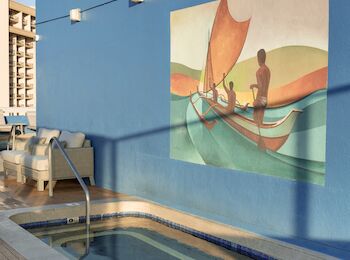A small, rectangular pool beside a blue wall featuring a mural of people in a boat with sails. There is poolside equipment and wooden decking.