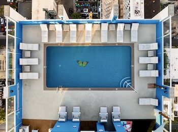 Aerial view of a rectangular rooftop pool surrounded by numerous lounge chairs, with a floating butterfly design in the water.